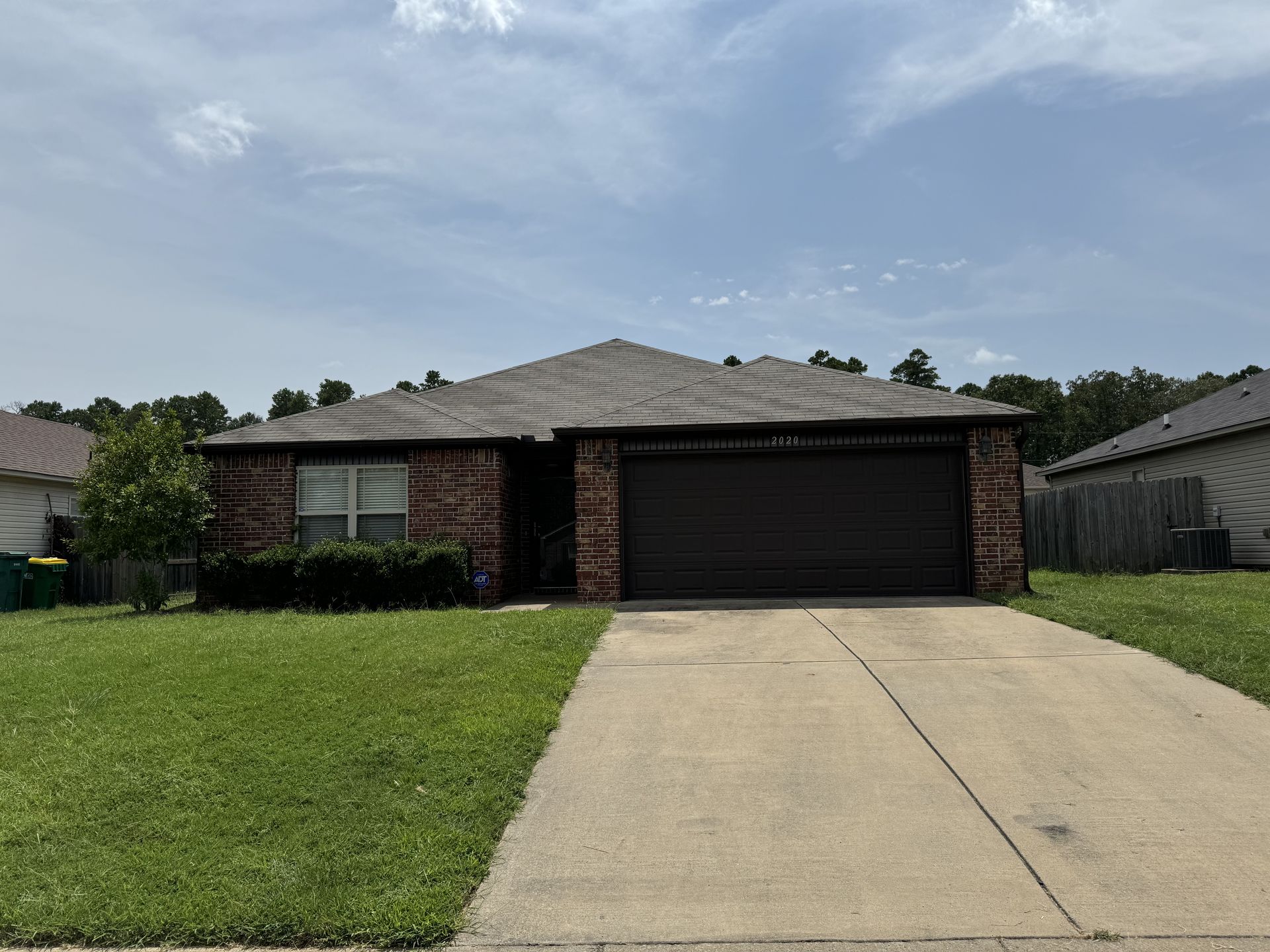 A brick house with a black garage door is for sale in a residential area.