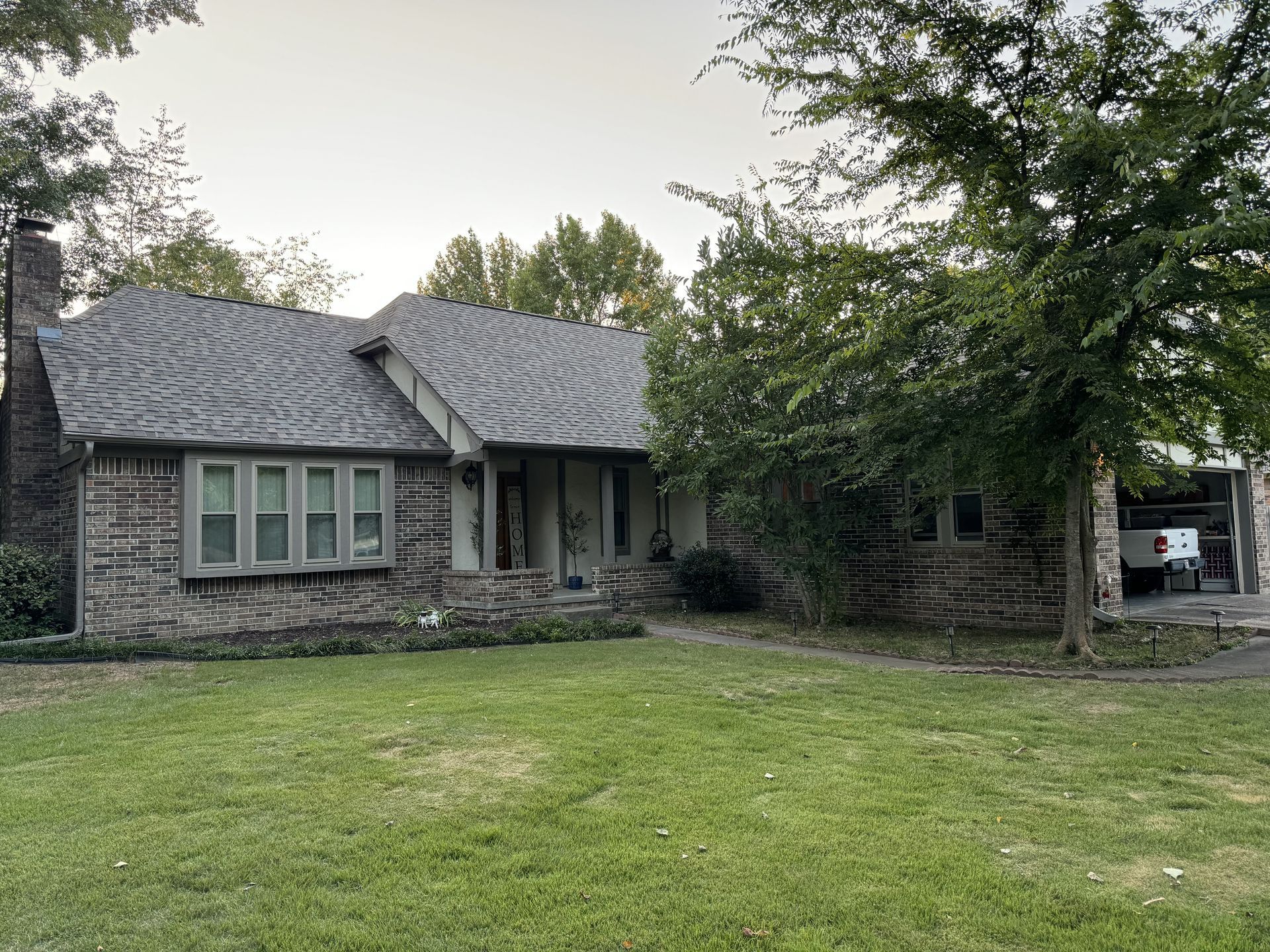 A brick house with a gray roof and a large lawn in front of it.