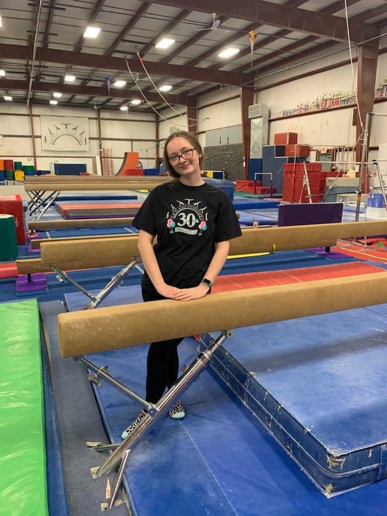 A woman is standing on a balance beam in a gym.