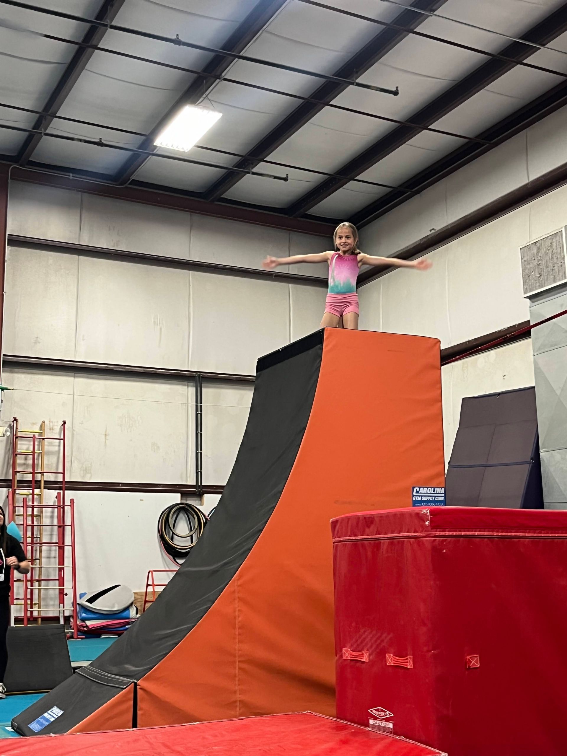 A little girl is standing on top of a ramp in a gym.