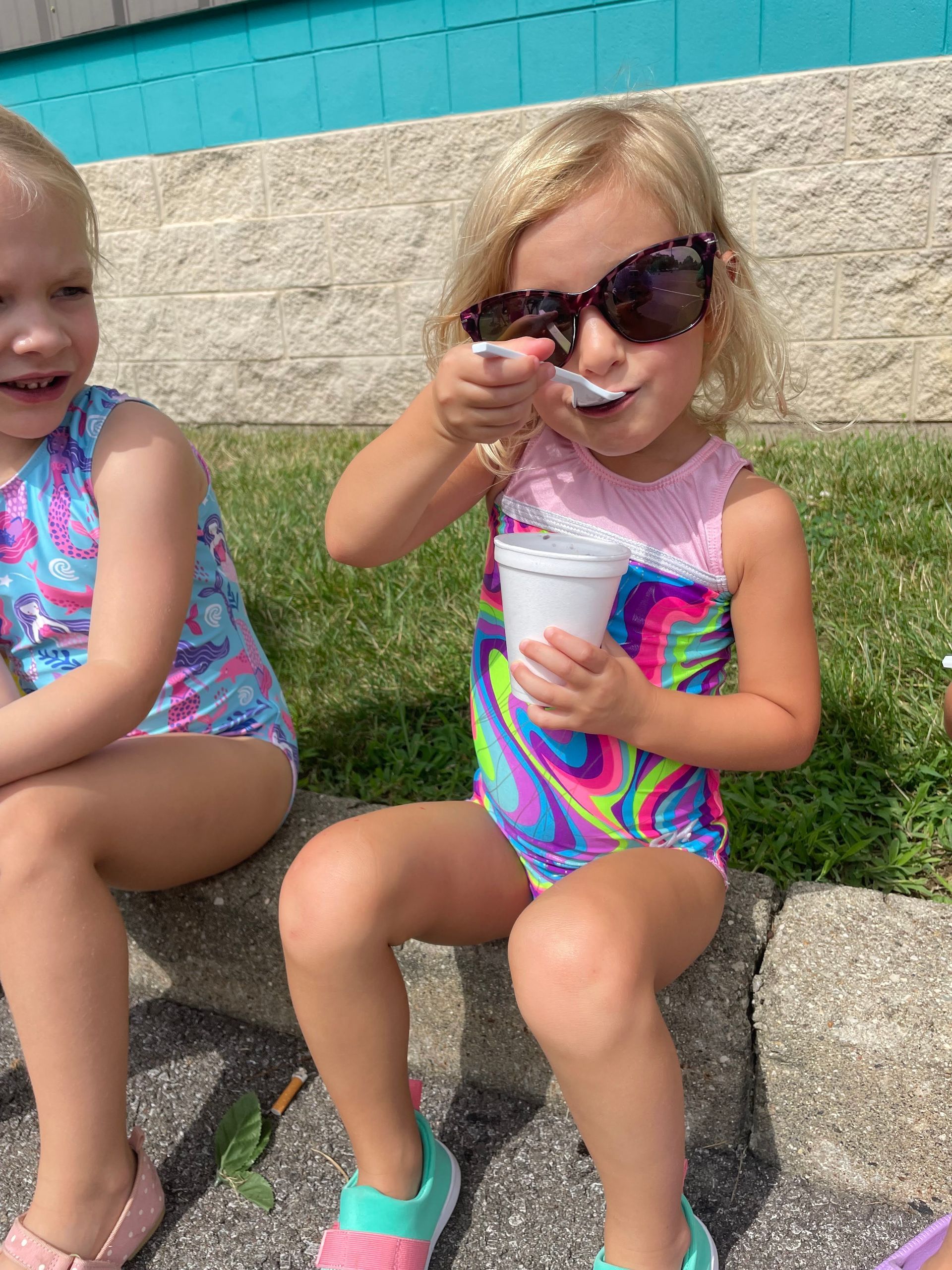 Two little girls are sitting on a sidewalk eating ice cream.