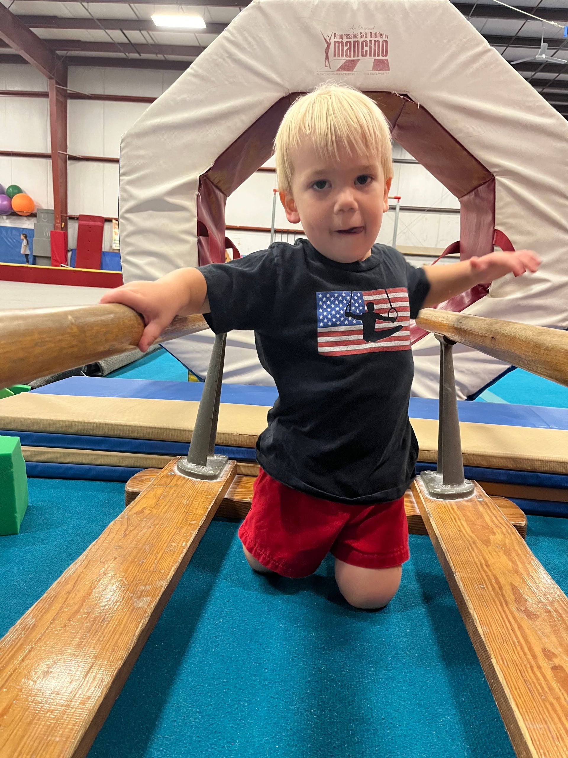 A young boy is kneeling on a balance beam in a gym.