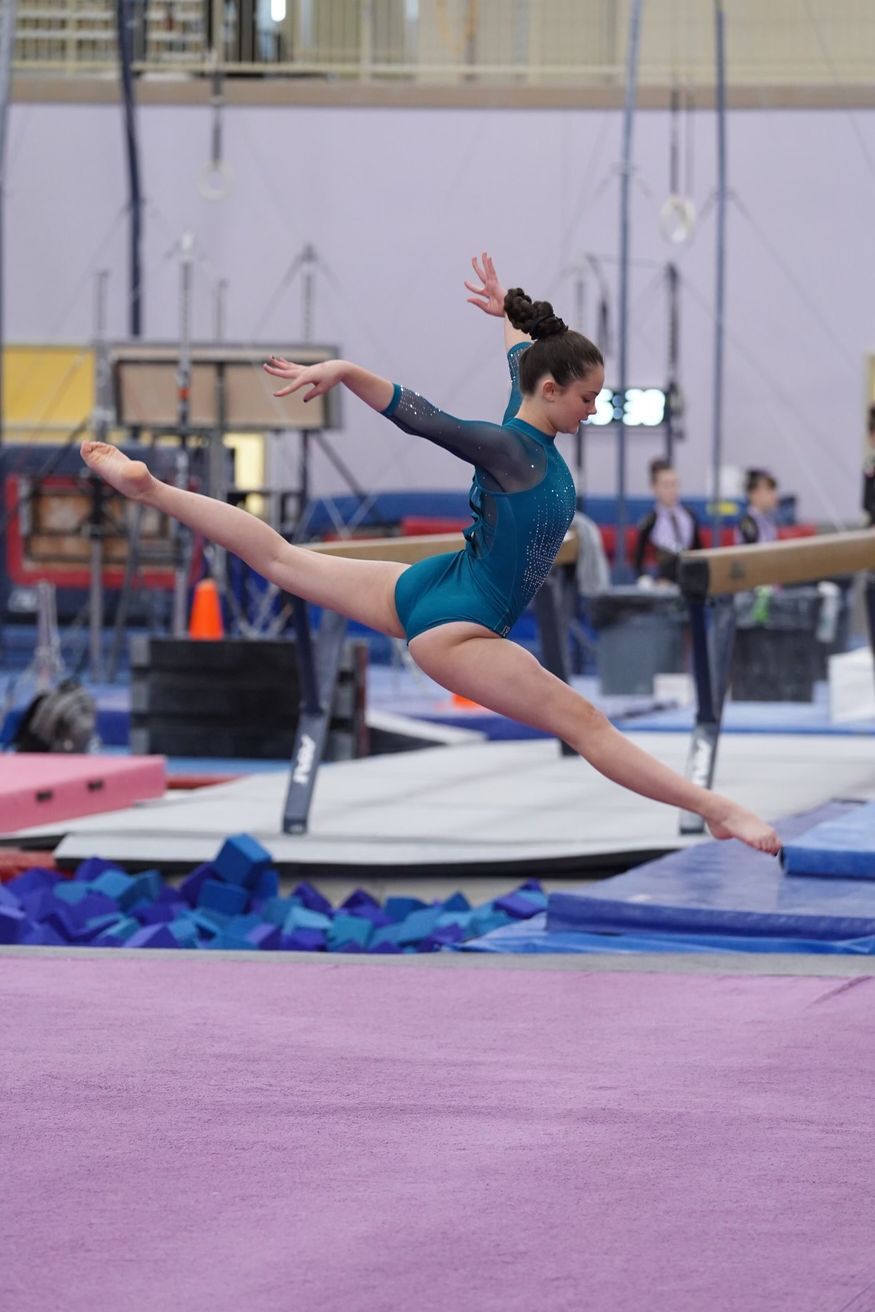 A female gymnast is doing a split on a balance beam.