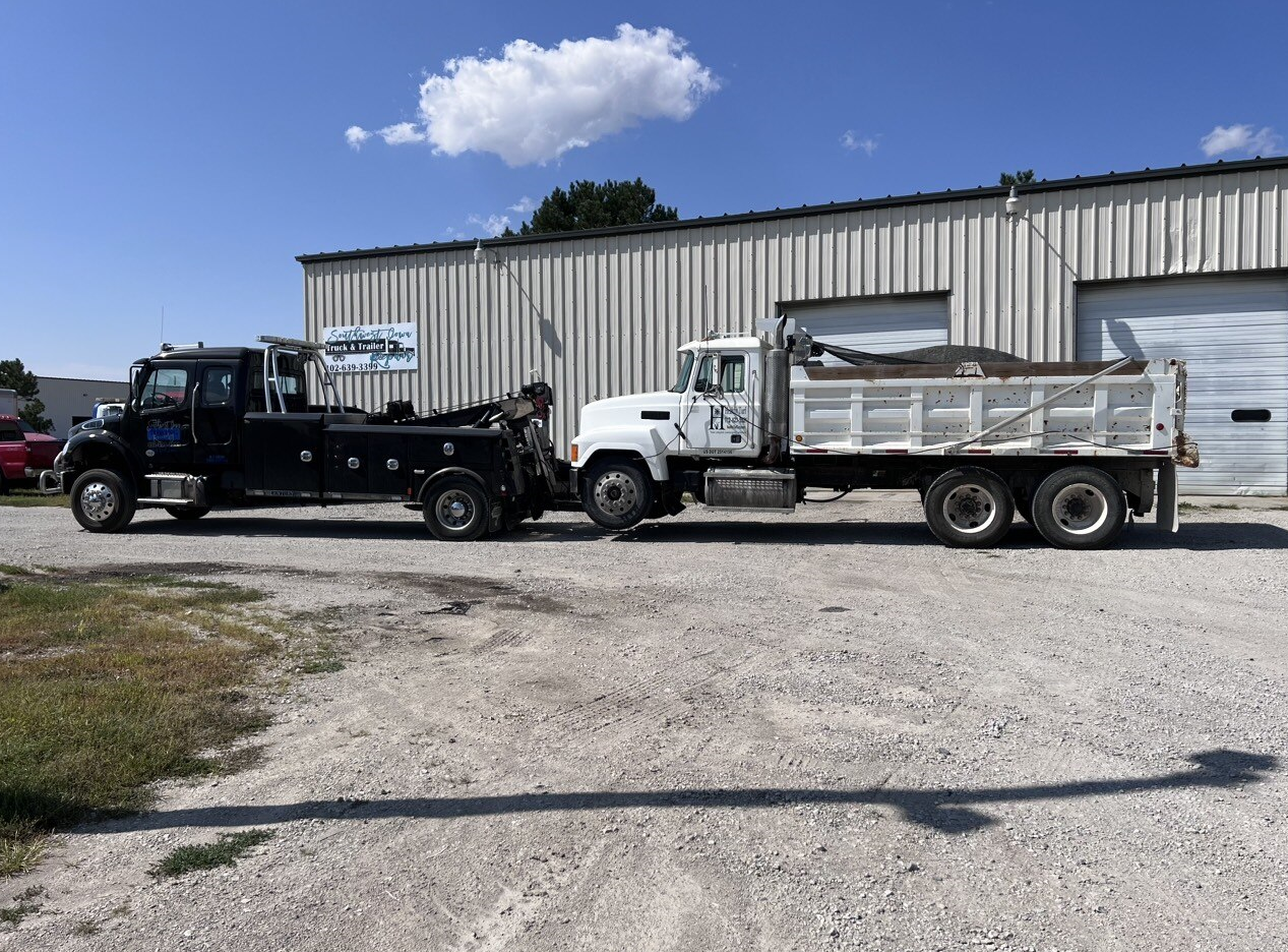 A tow truck and a dump truck are parked in front of a building.