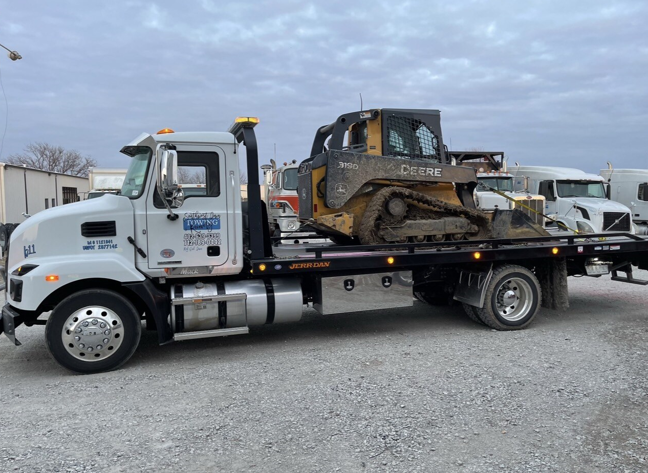 A tow truck is carrying a bulldozer on the back of it.