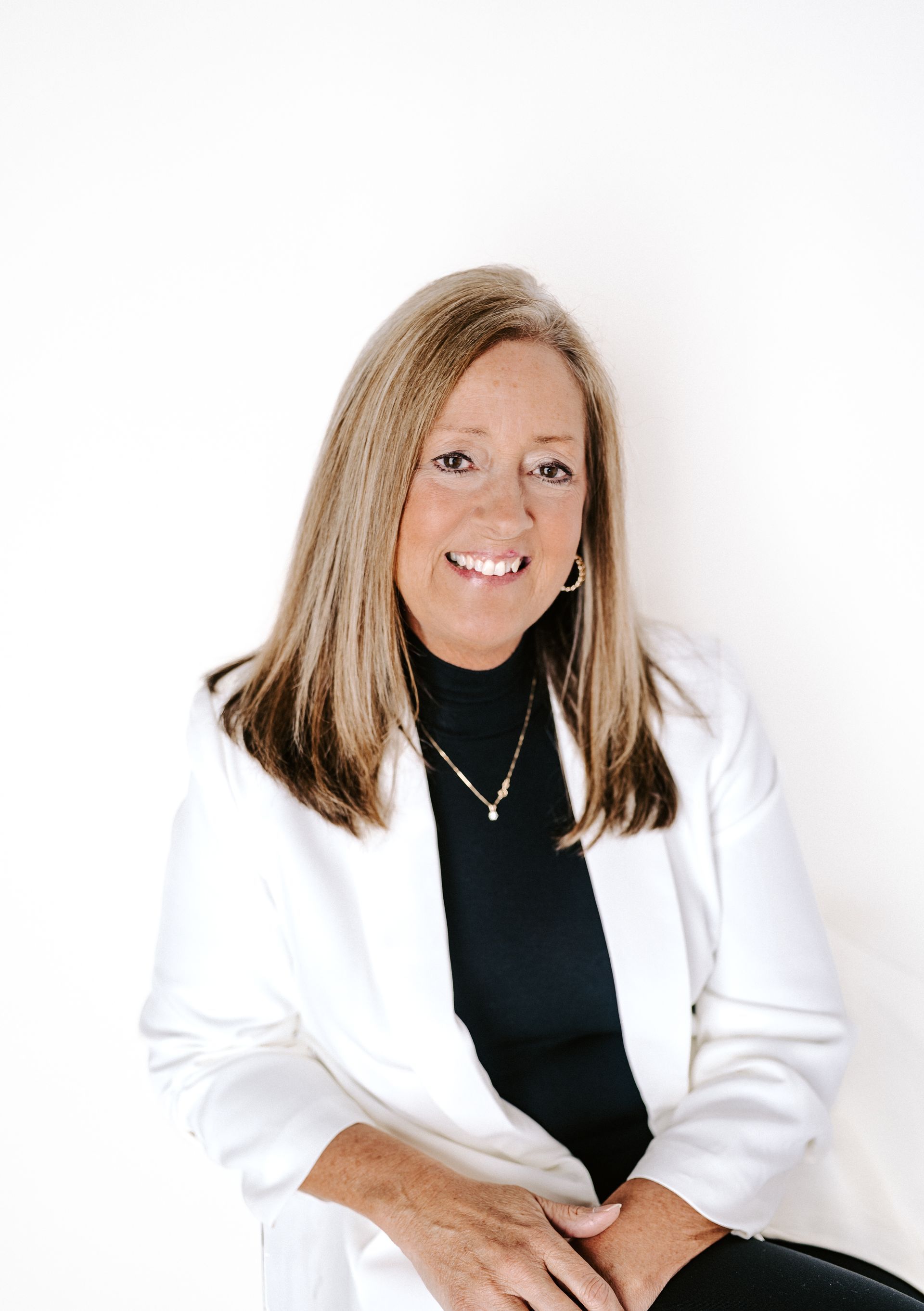 A woman is wearing a white jacket and a black turtleneck.