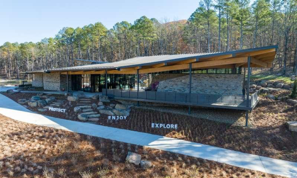 A large stone building with a wooden roof is in the middle of a forest.