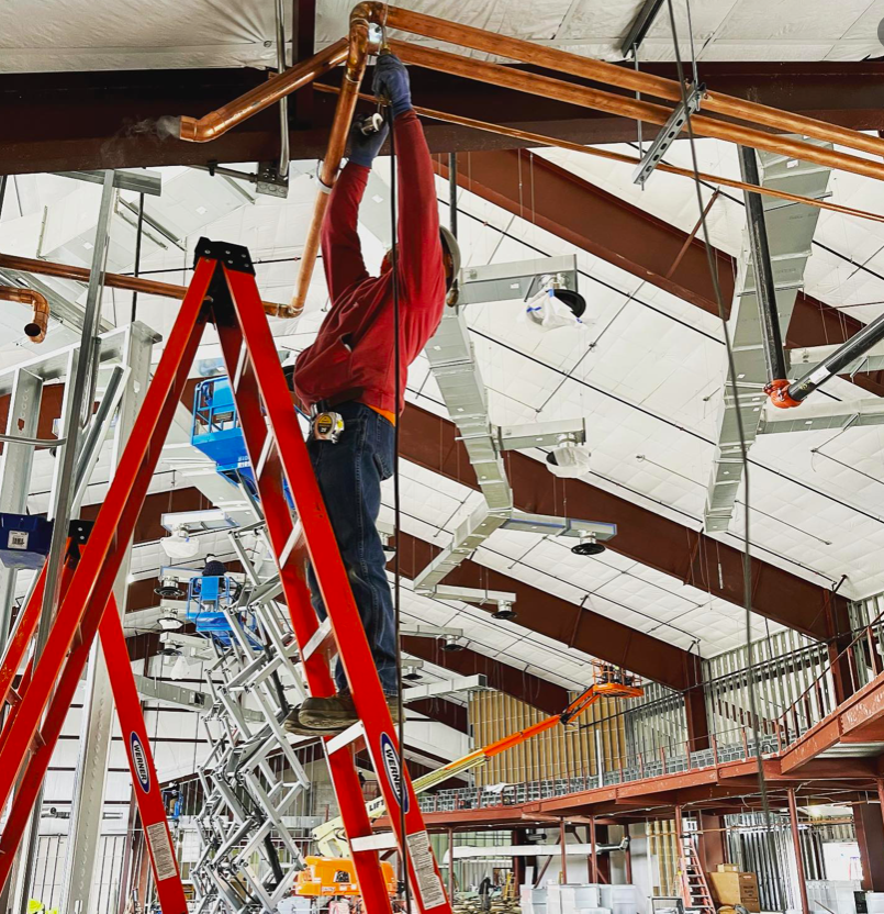 A man is standing on a red ladder working on pipes