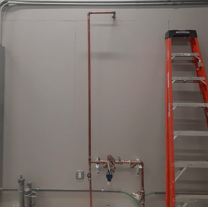 An orange ladder is sitting next to a copper pipe