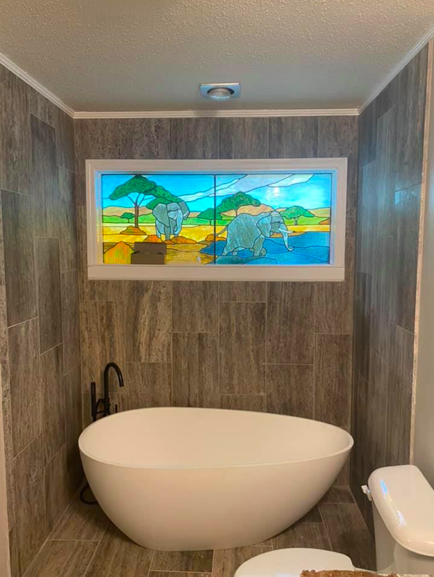 A bathroom with a bathtub and a window with elephants on it.