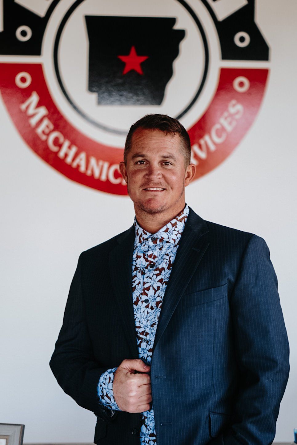 A man in a suit is standing in front of a mechanic services logo.