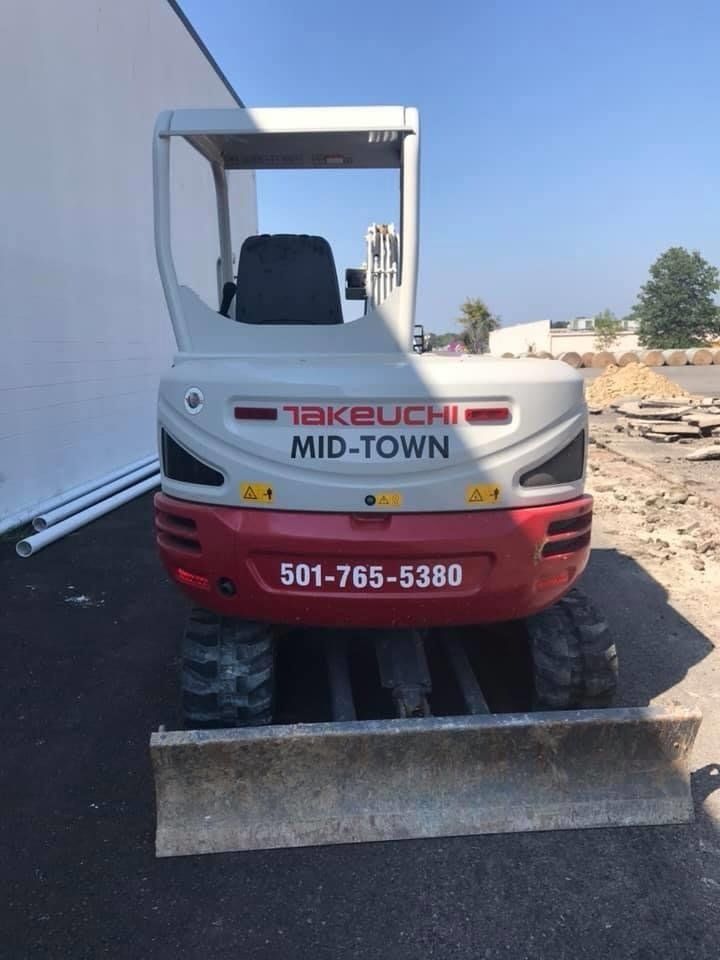 A takeuchi mid-town bulldozer is parked in front of a building