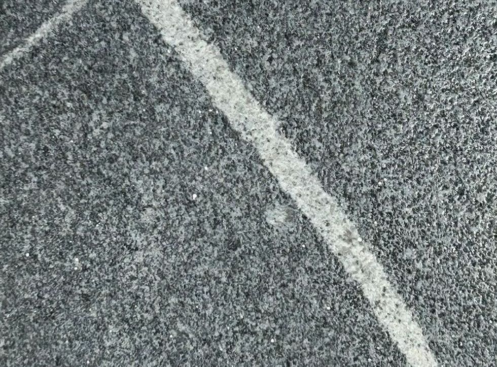 A black tile with a green star on it is sitting on a concrete surface.