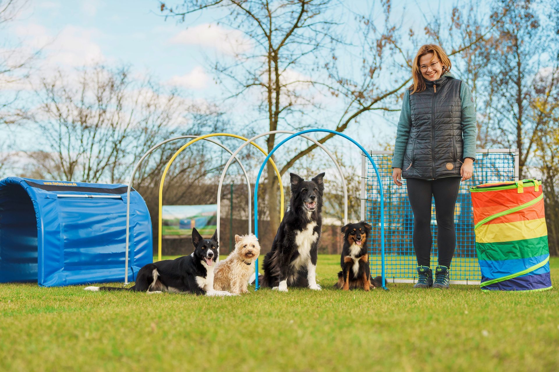Eine Frau steht neben einer Gruppe Hunde auf einem Feld.