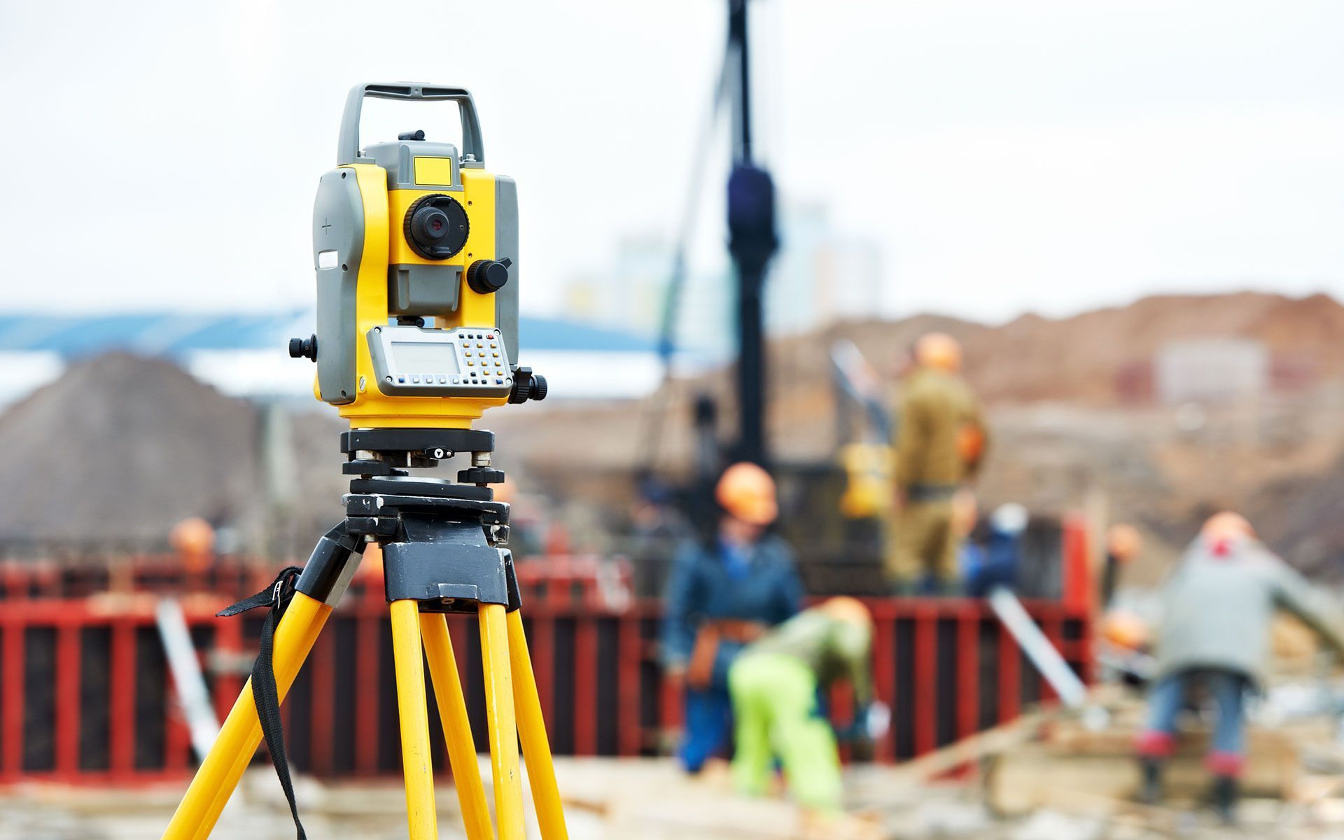 A yellow theodolite is sitting on a tripod on a construction site.