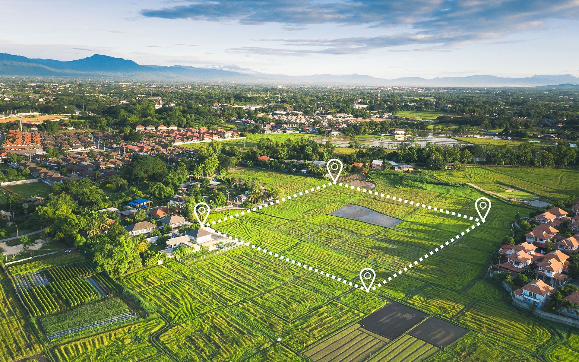 An aerial view of a lush green field with a village in the background.