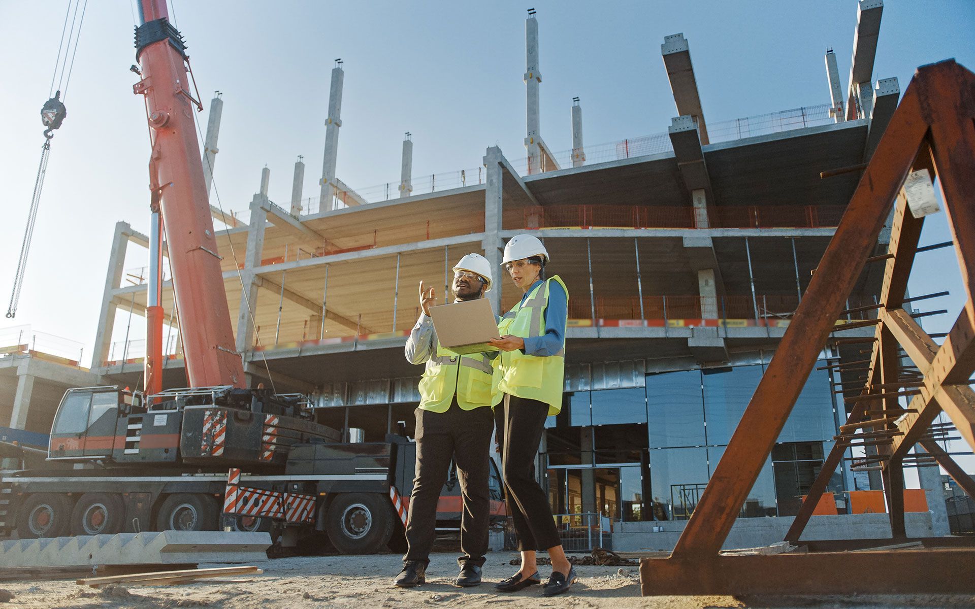 Two construction workers are walking on a construction site looking at a blueprint.