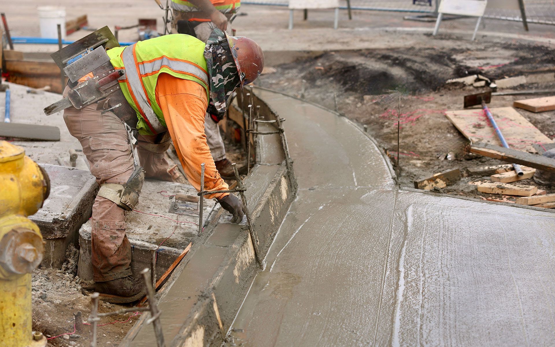 A construction worker is pouring concrete on a sidewalk.