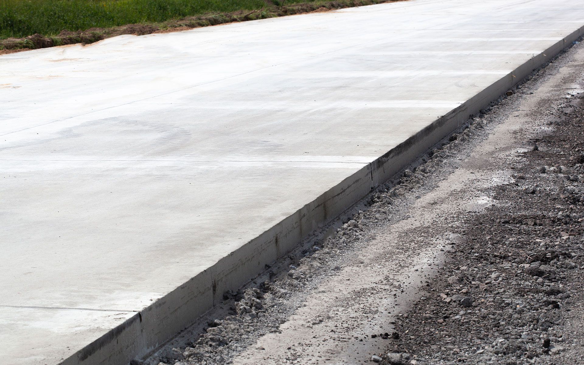 A close up of a concrete driveway with gravel on the side