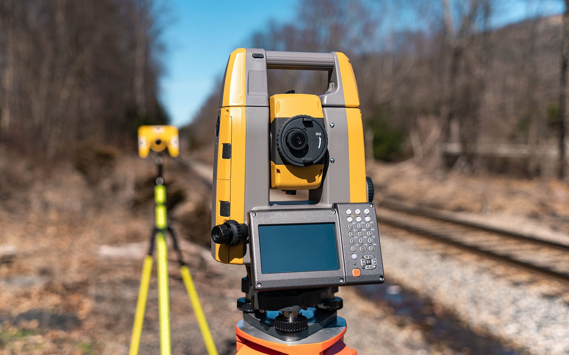 A yellow theodolite is sitting on top of a tripod next to a train track.