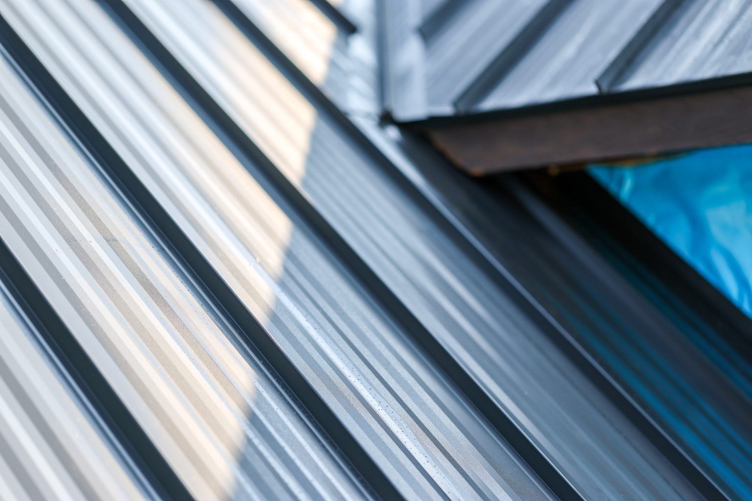 Close-up of a dark grey metal standing seam roof with a blue tarp visible under an open roof section.