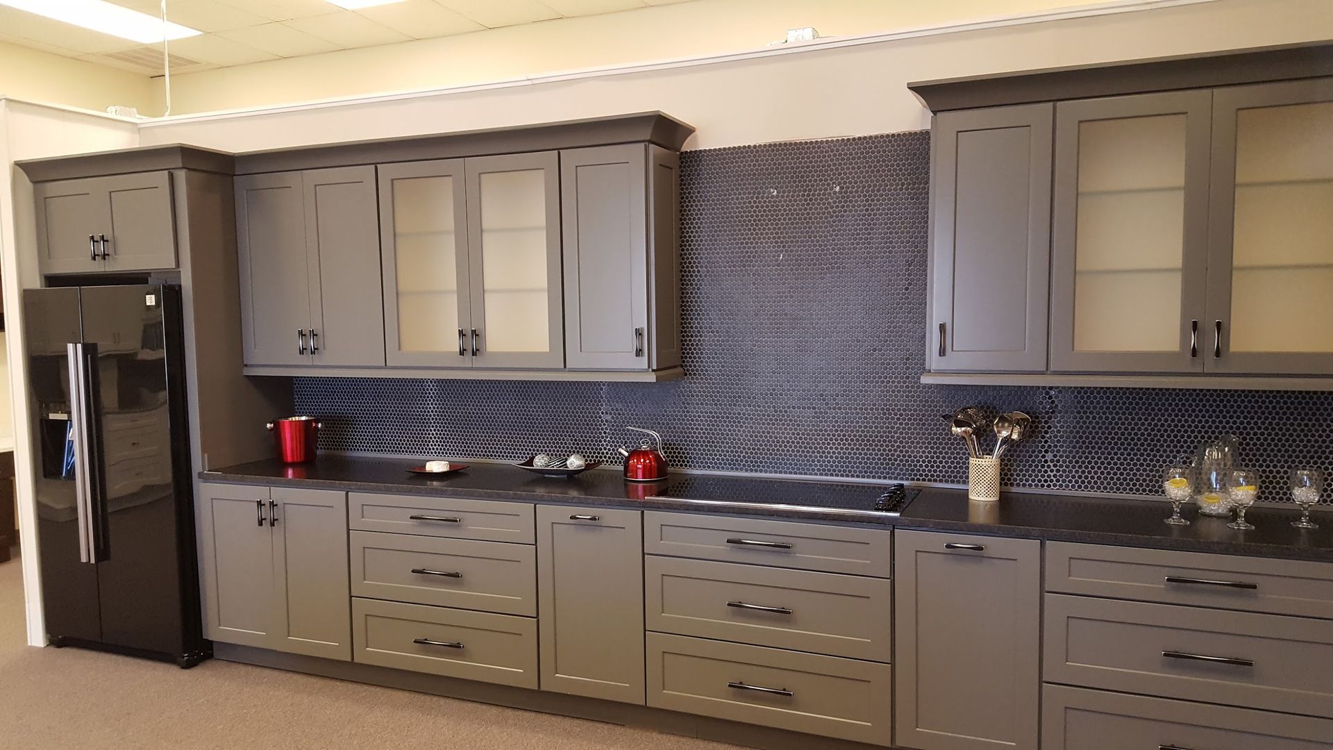 Gray kitchen cabinets with black countertop and backsplash, with a black refrigerator.