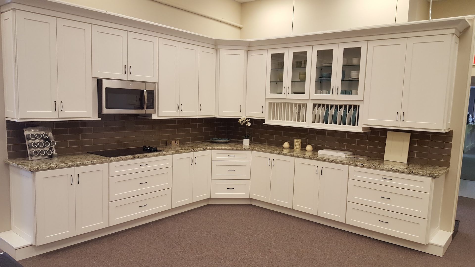 White kitchen cabinets with granite countertops and a brown tile backsplash.