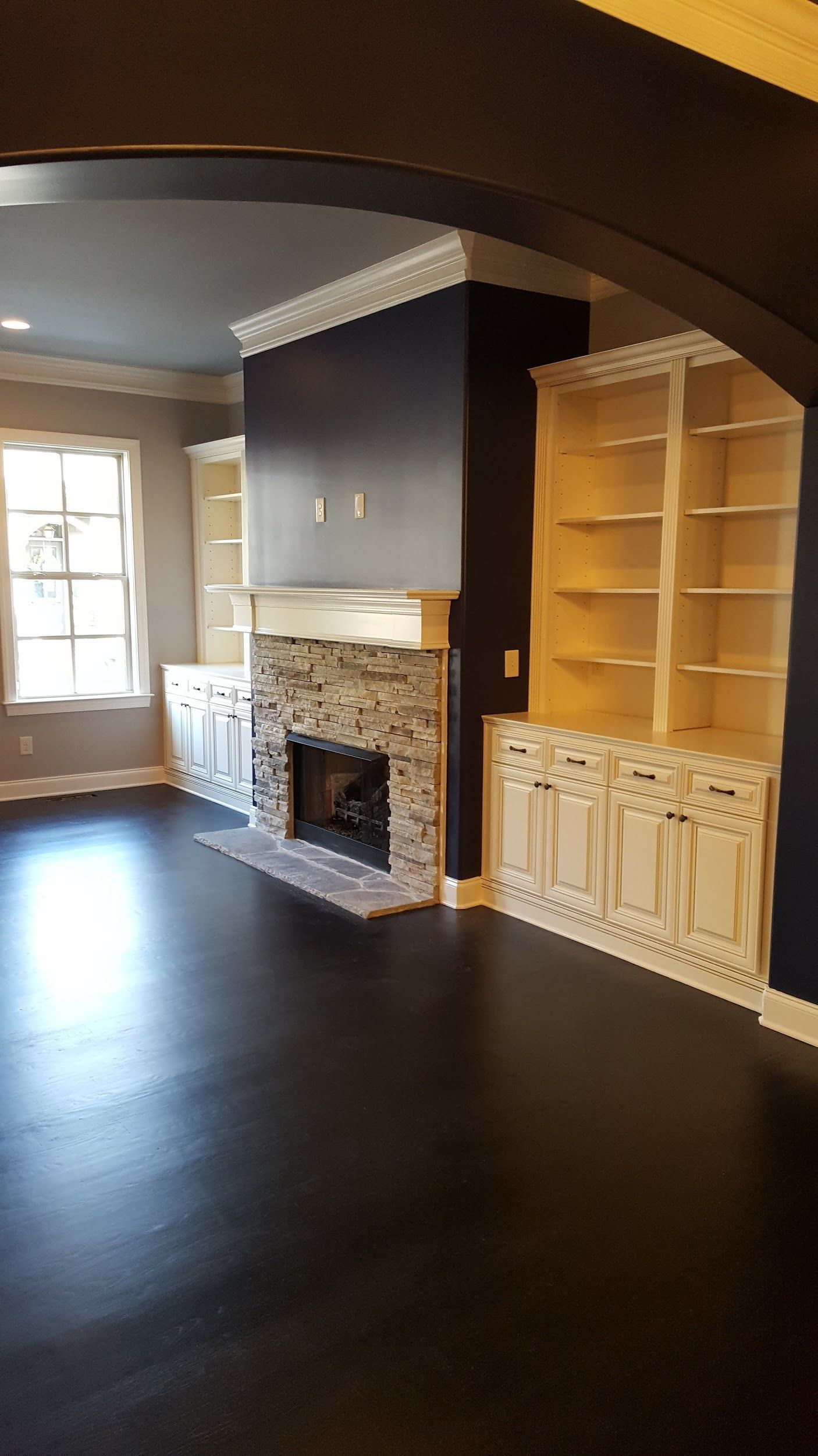 Living room with fireplace, built-in shelving, dark blue walls, white trim, and dark wood floors.