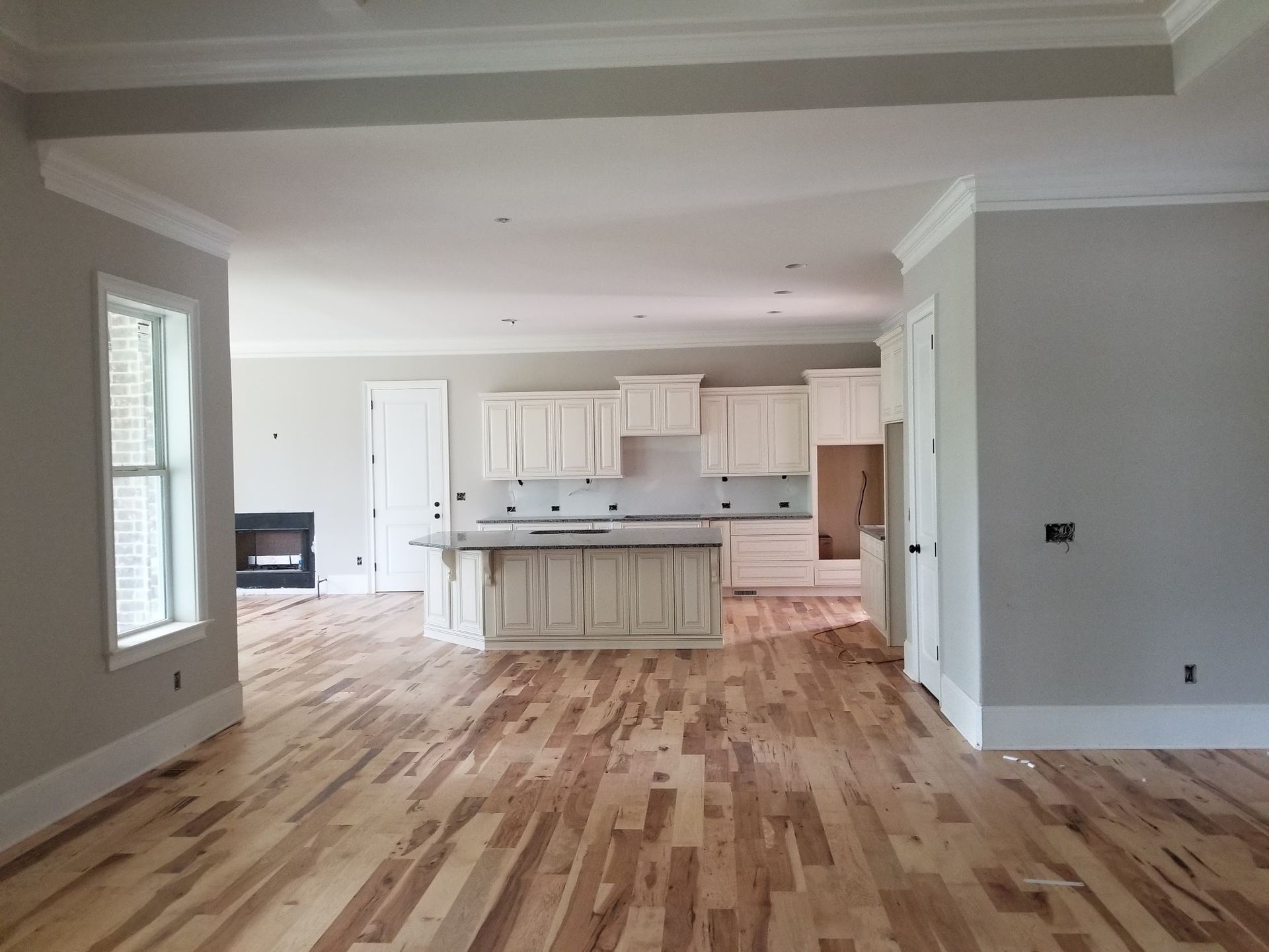 Spacious interior with hardwood floors, a kitchen, and a fireplace. Neutral walls and white cabinets create a bright feel.