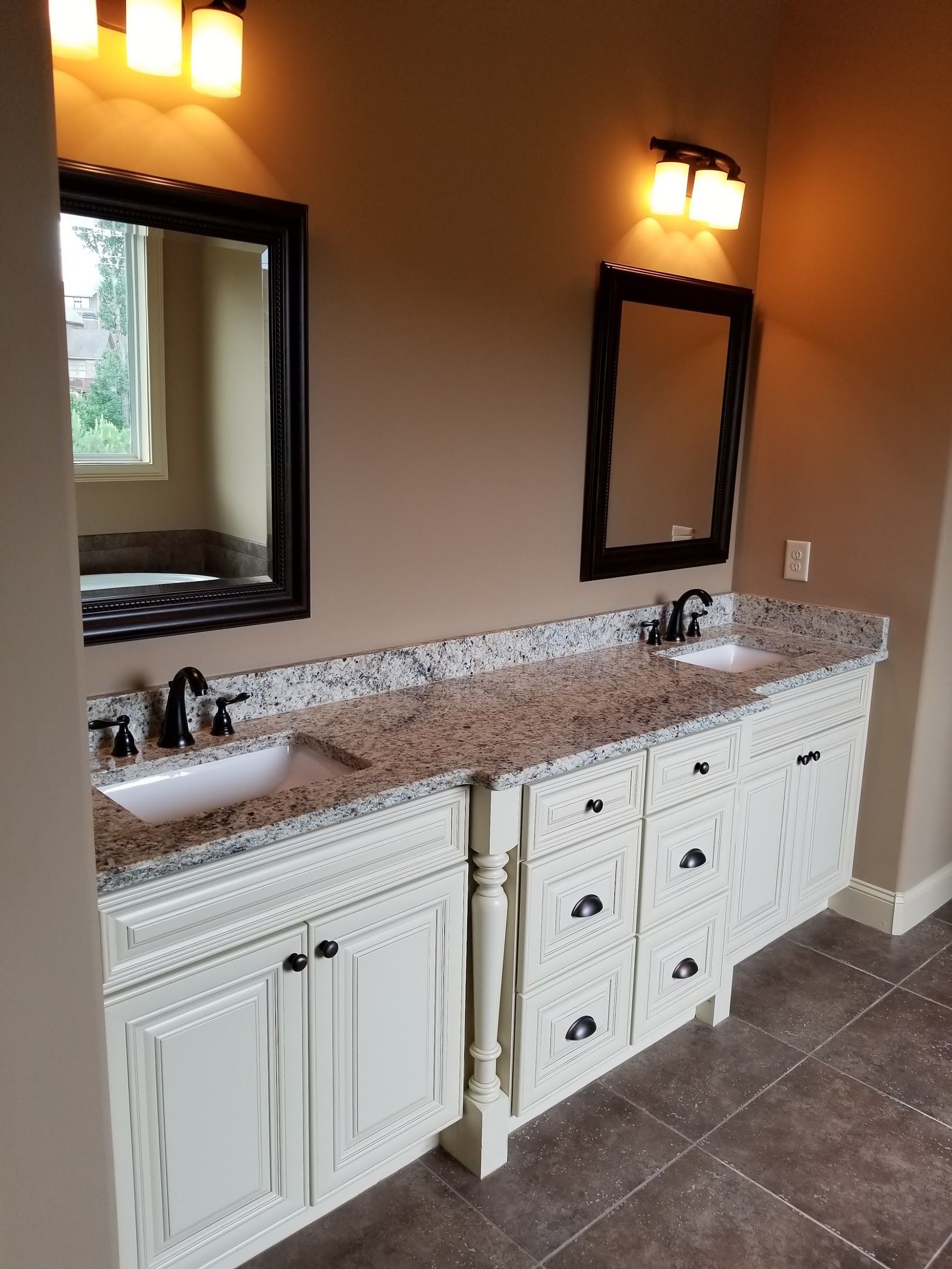 Two white vanities with granite countertops, sinks, mirrors, and sconces against a beige wall.