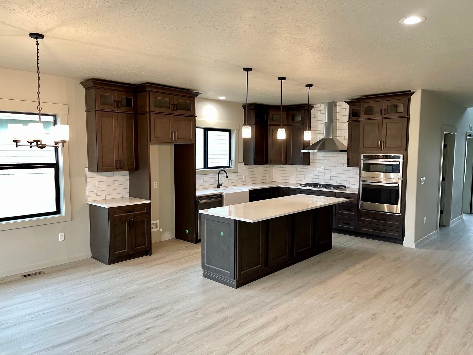 Modern kitchen with dark cabinets, white countertops, and light wood-look flooring.