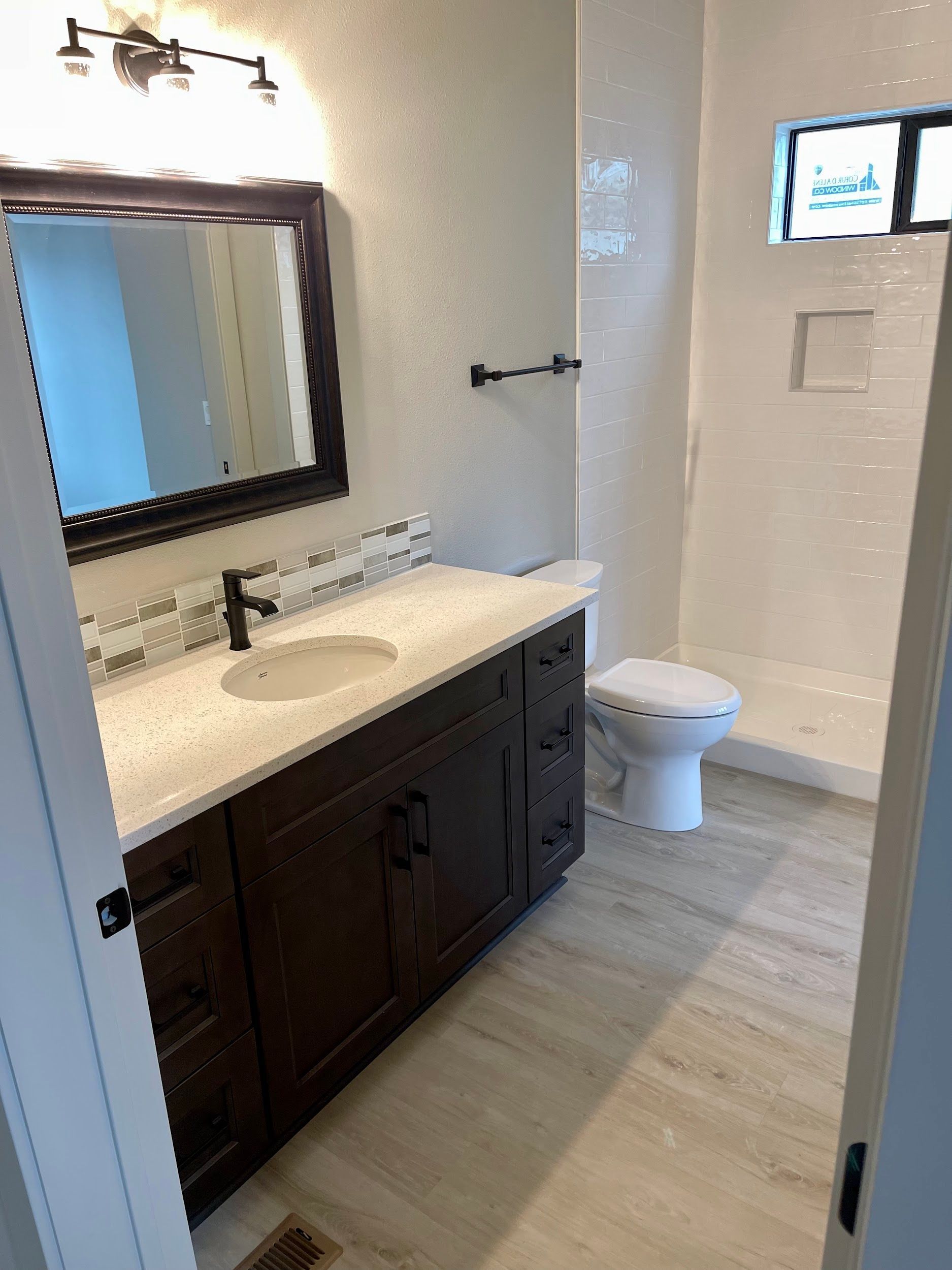 Bathroom with dark brown vanity, white countertop, and walk-in shower with a window.