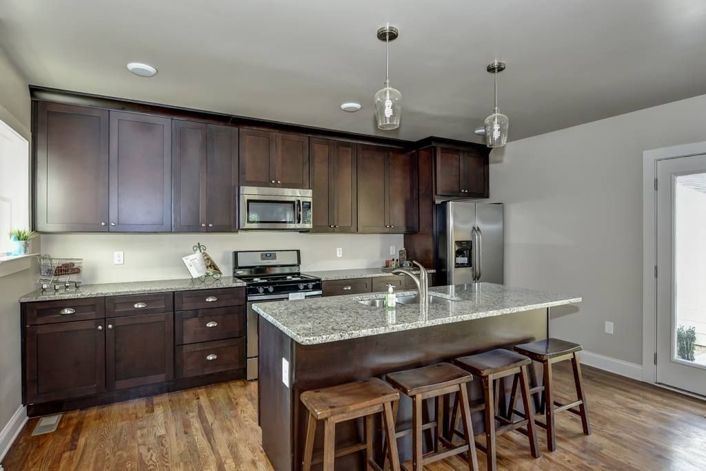 Kitchen with dark wood cabinets, granite countertops, and a stainless steel refrigerator and appliances. Island with stools.