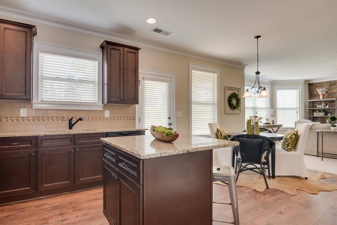 Kitchen with dark brown cabinets, island, and dining area. Hardwood floor, granite countertops.