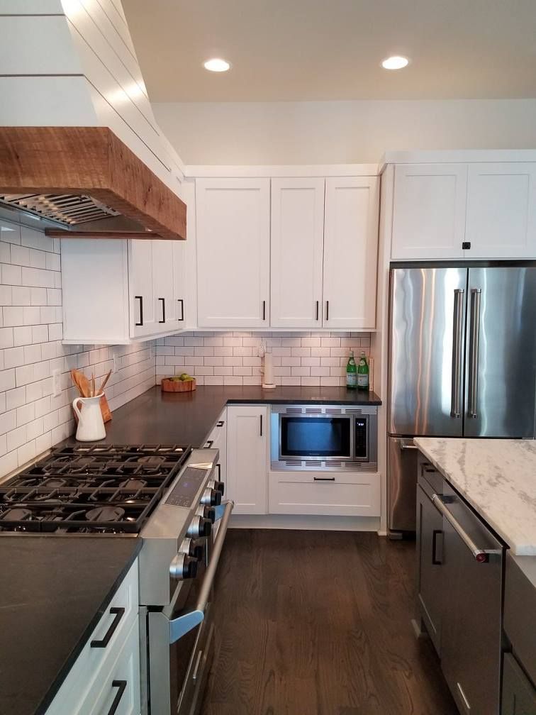 Modern kitchen with white cabinets, stainless steel appliances, dark countertops, and a dark wood floor.