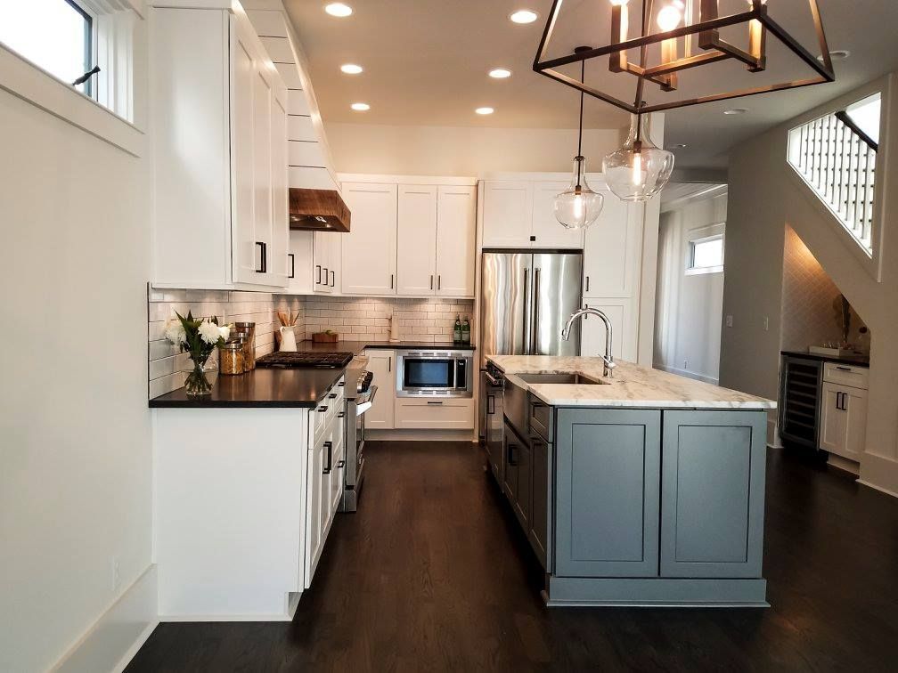 Modern kitchen with white cabinets, dark island, stainless steel appliances, and hardwood floors.