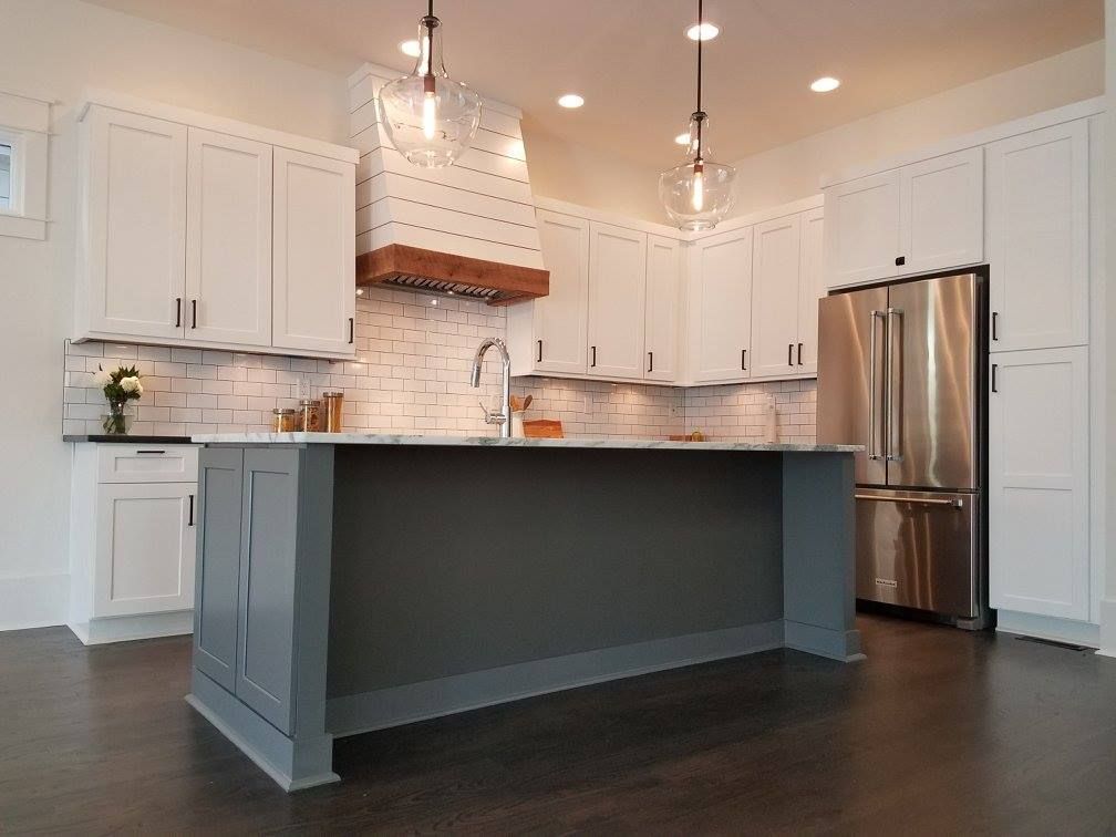 Modern kitchen with white cabinets, gray island, stainless steel appliances, and dark wood floors.