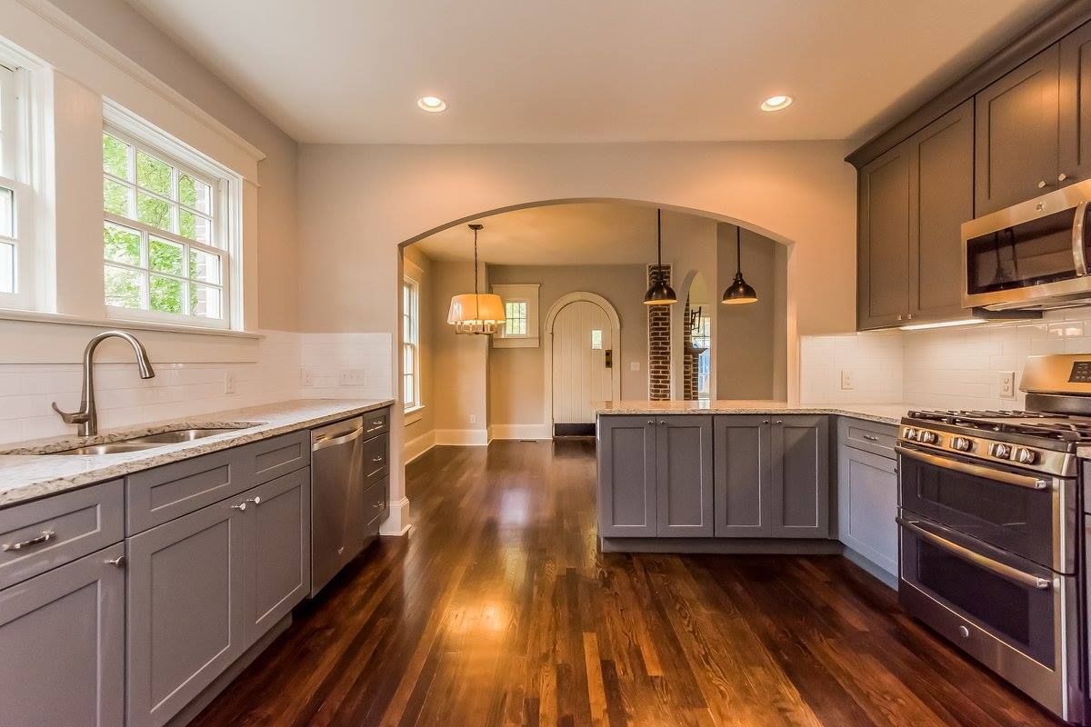 Kitchen with gray cabinets, white countertops, and wooden floors, leading to another room.