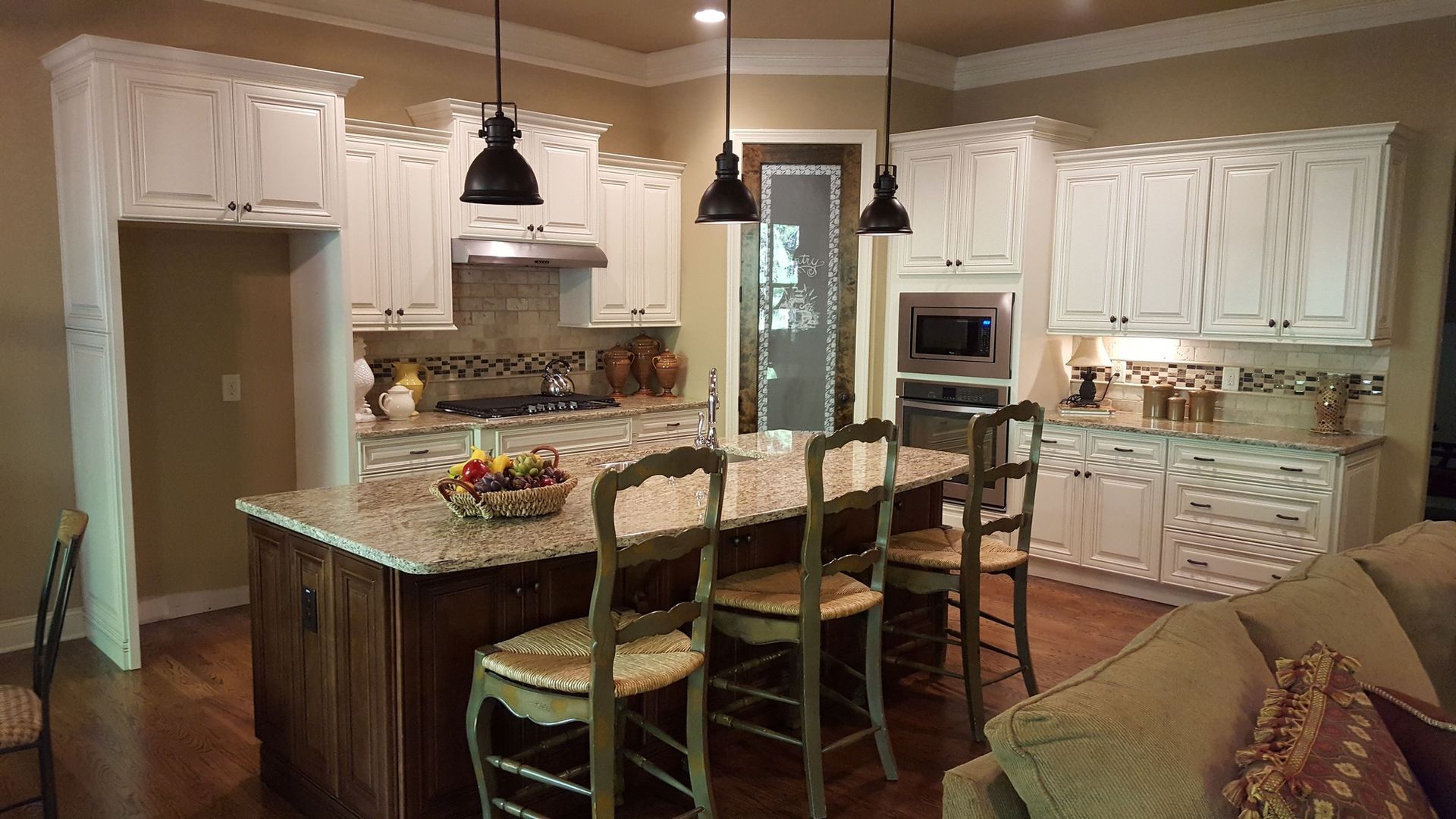 Kitchen with white cabinets, island with seating, and hanging pendant lights.
