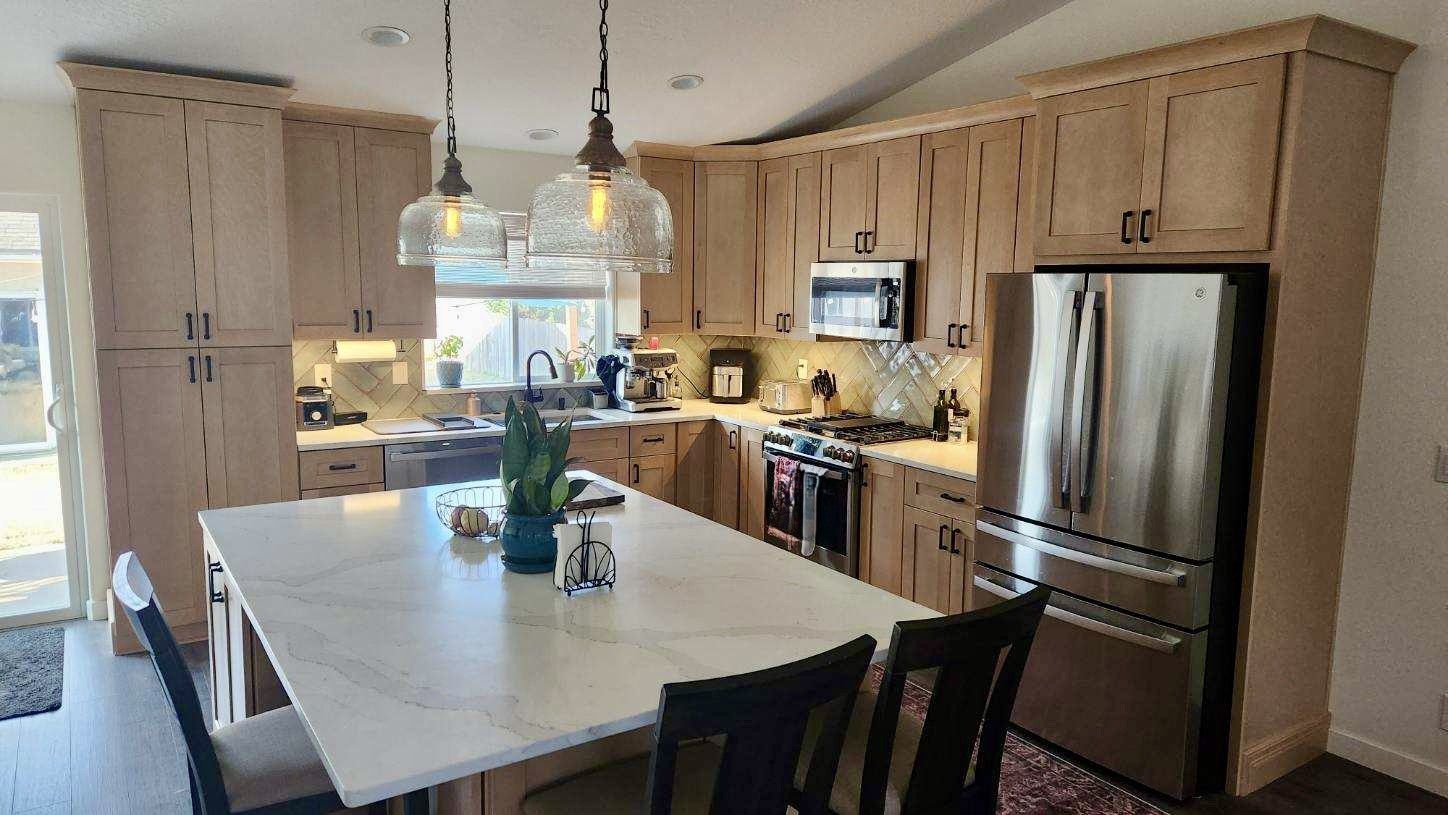 Light-colored kitchen with island, stainless steel appliances, and pendant lights. Cabinets in natural wood tones.