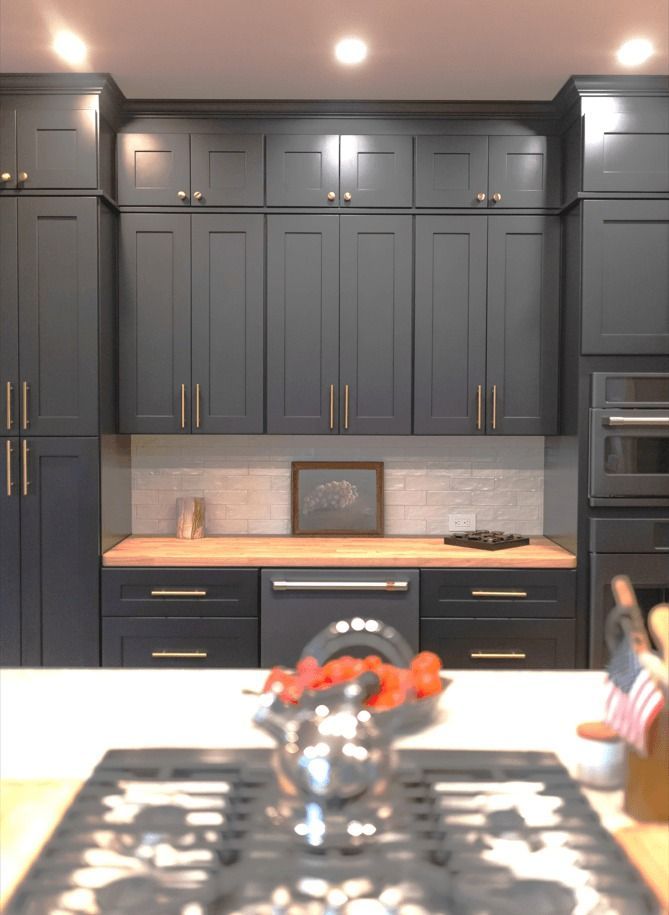 Dark blue kitchen with wood countertops, stainless steel appliances, and a central stovetop.