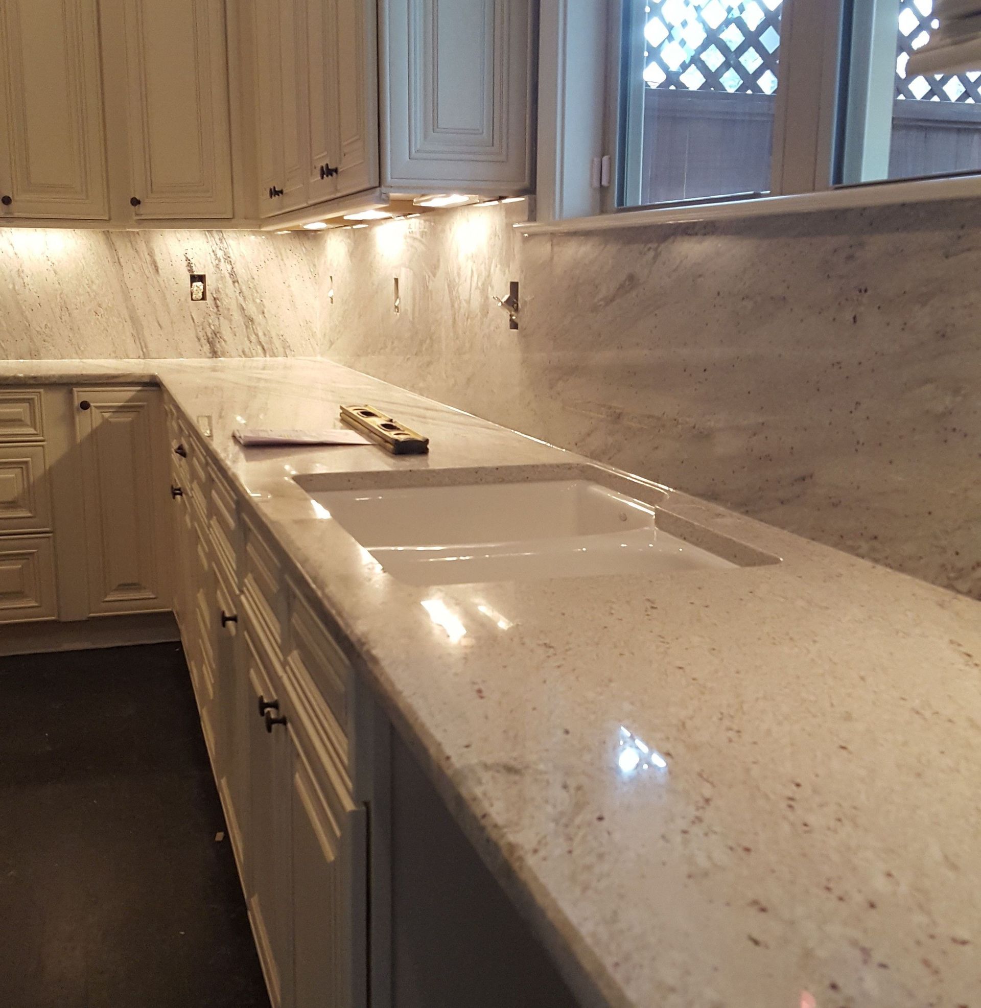 Cream-colored kitchen with countertops and cabinetry, a built-in sink, and under-cabinet lighting.
