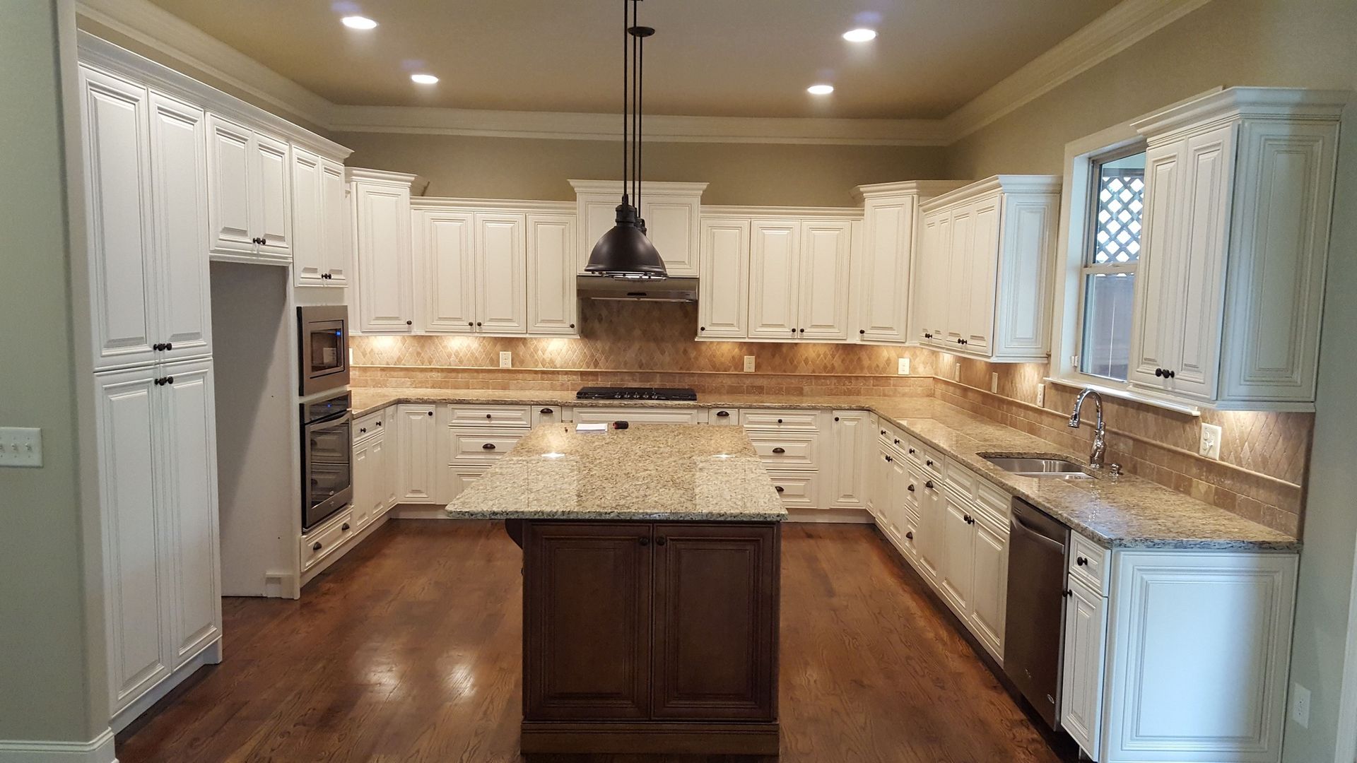 White kitchen cabinets with granite countertops and a dark wood island on a hardwood floor.