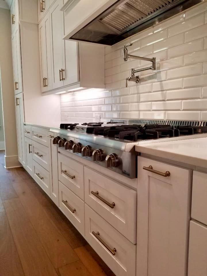 White kitchen with stove, cabinets, and backsplash; brass hardware on cabinets, wood floor.