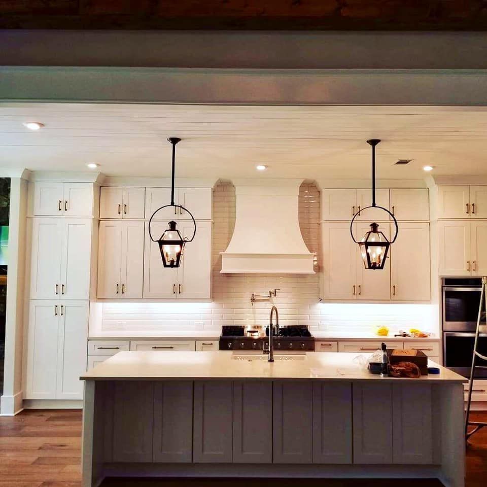 White kitchen with island, cabinets, stove, range hood, and hanging lanterns.