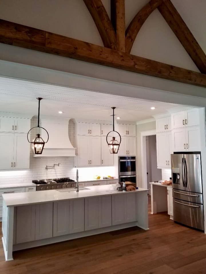 White kitchen with island, pendant lights, stainless steel appliances, and wooden beams.