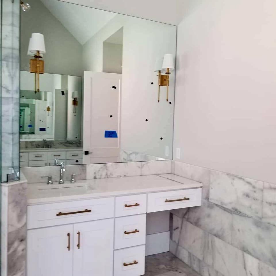 Bathroom with a white vanity, marble walls, large mirror, and gold sconces.