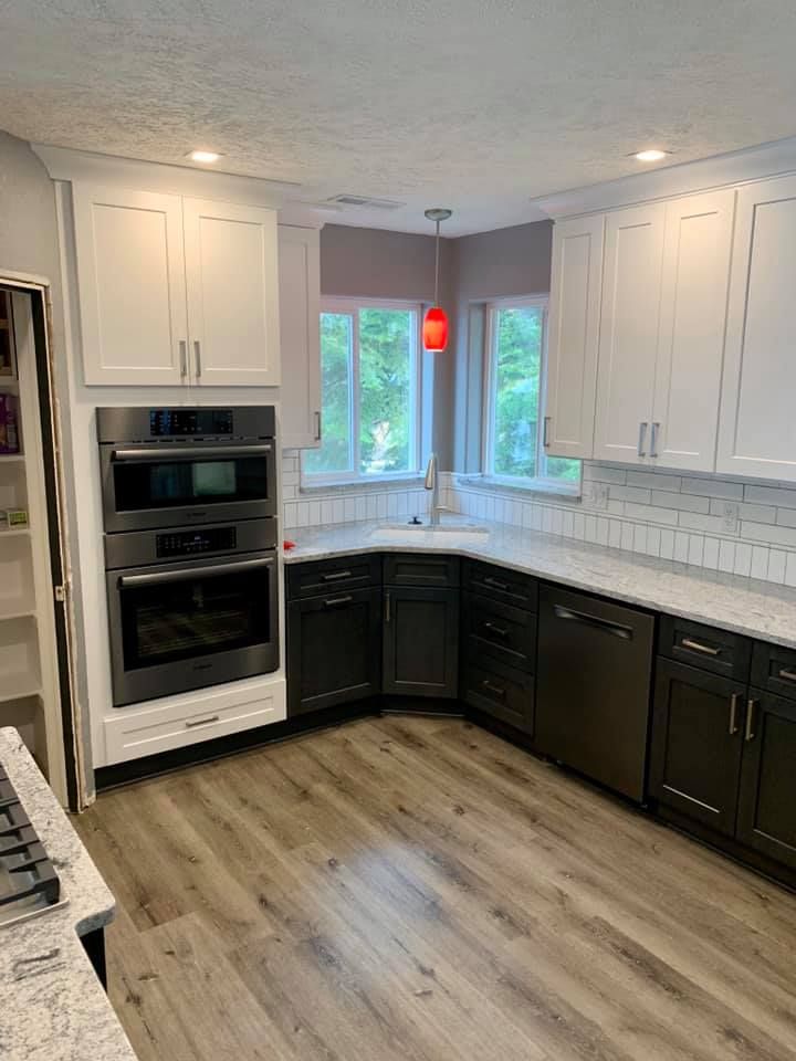 Modern kitchen with white upper cabinets, dark lower cabinets, and wood-look flooring.