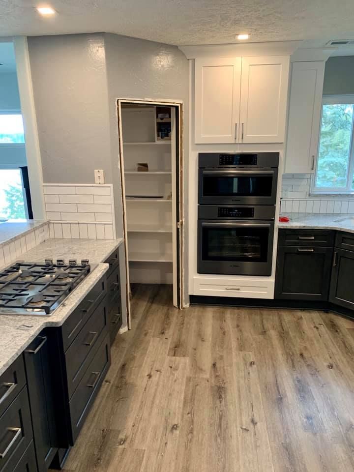 Kitchen with white and gray cabinets, pantry, built-in oven, gas stove, and light wood flooring.