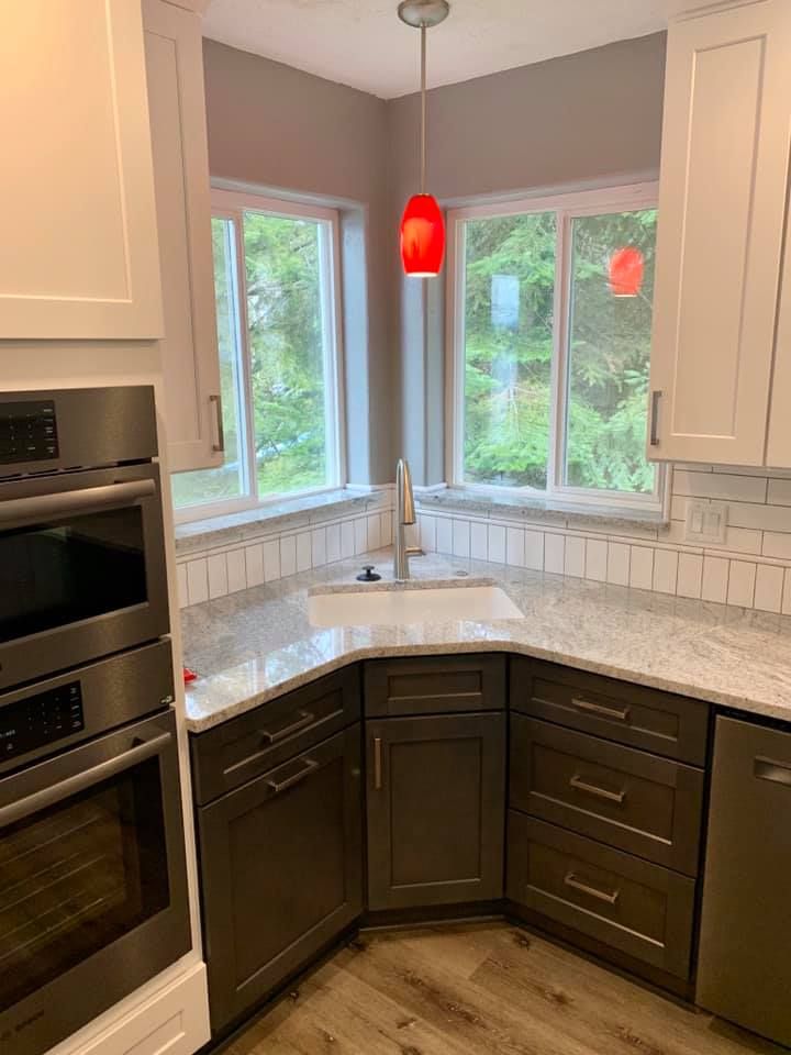 Modern kitchen with white and dark gray cabinets, granite counters, and a window above the sink. Red pendant lights.
